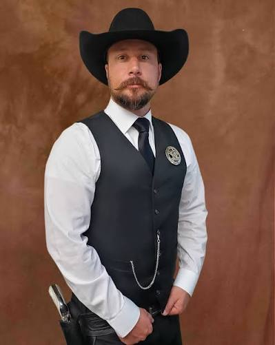 James Maiorano III wearing a cowboy hat, vest, badge, and holstered firearm